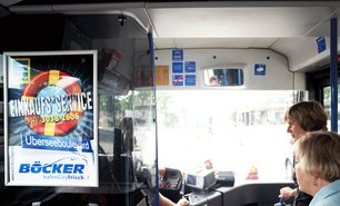 Blick in den vorderen Bereich eines Busses mit digitaler Anzeige und Werbeplakat hinter dem Fahrer. Verkehrsmittelwerbung wird hier gezielt im Sichtfeld der Fahrgäste platziert.