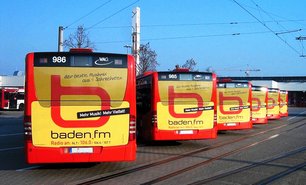 Mehrere Stadtbusse mit einheitlichem Werbemotiv auf der Rückseite stehen nebeneinander. Verkehrsmittelwerbung sorgt hier für hohe Sichtbarkeit im urbanen Raum.