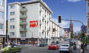 Innenstadt mit stark frequentierter Kreuzung. An einem Wohnhaus befindet sich ein auffälliges Großflächen Plakat mit roter Farbgestaltung direkt über der Ampel.