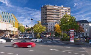 Litfaßsäule im Straßenverkehrsknotenpunkt vor Bürogebäuden – auffällige Werbung an einer gut frequentierten Allgemeinstelle.