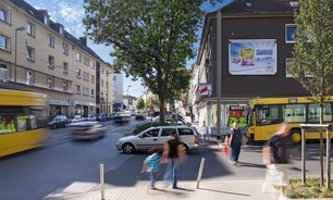 Abendliche Kreuzung mit leuchtenden Rücklichtern. Rechts im Bild ein gut beleuchtetes Plakat (Großfläche) an einer Hauswand für maximale Sichtbarkeit im Dunkeln.