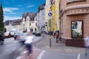 Belebte Innenstadt mit einem City Light Poster (CLP) an einer Hausfassade – aufmerksamkeitsstarke Werbefläche für Fußgänger und Radfahrer im urbanen Umfeld.